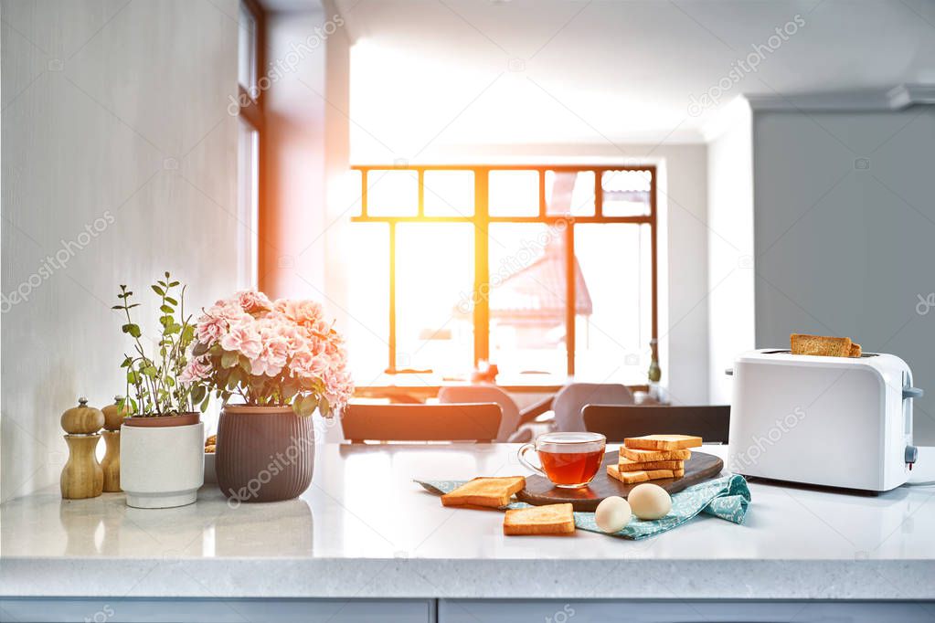 Breakfast in the cozy kitchen. Useful and tasty food. Tea and toast in a toaster, eggs. Sun flare