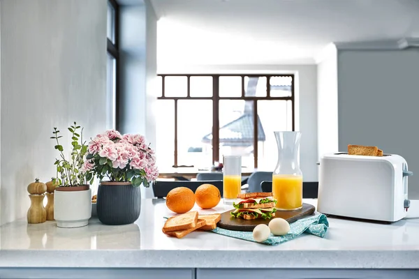 Elektrisk batong brödrost med apelsinjuice med smörgås på köksbordet. Frukost i det mysiga köket. — Stockfoto