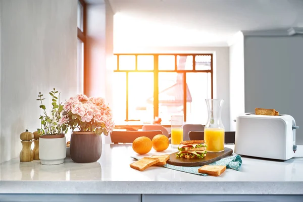 Elektrisk batong brödrost med apelsinjuice med smörgås på köksbordet. Frukost i det mysiga köket. Solen flare — Stockfoto