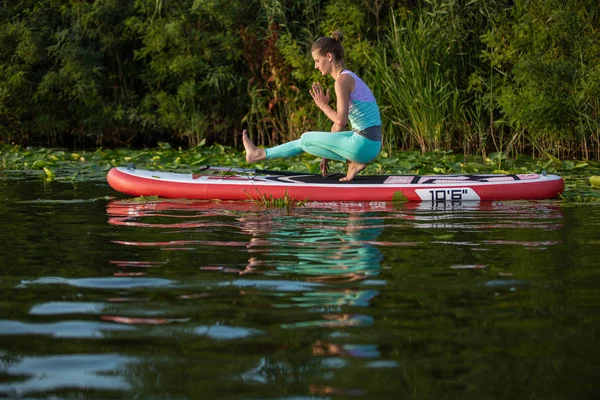 Junge Frau macht Yoga auf einem Stand Up Paddle Board sup auf einem schönen See oder Fluss — Stockfoto