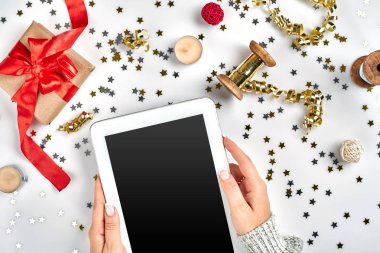 Beyaz zemin üzerinde yatıyordu, en iyi görünüm Noel kompozisyon düz. Dijital tablet, hediye kutusu ile kırmızı kumaş teyp, sarmal şerit, altın boncuk, konfeti yıldız.