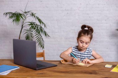 Sevimli küçük kız onu laptop ve defter ile masada oturuyor