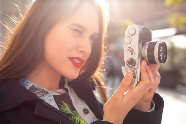 Ευτυχισμένος hipster κορίτσι κάνει φωτογραφία με ρετρό κάμερα στην πόλη δρόμο. Ήλιος φωτοβολίδα — Φωτογραφία Αρχείου