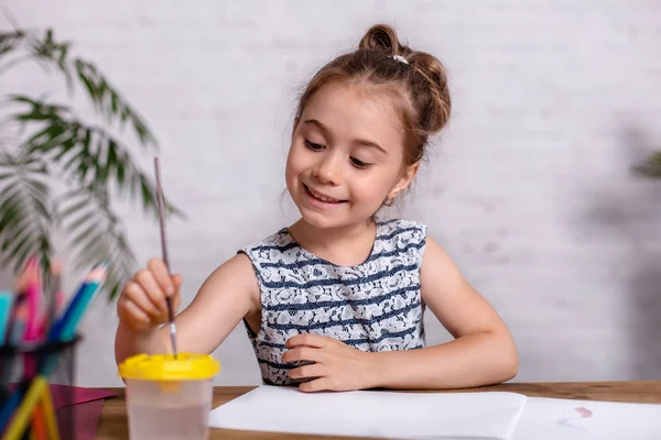 Вдохновлённая маленькая девочка за столом рисовала красками — стоковое фото
