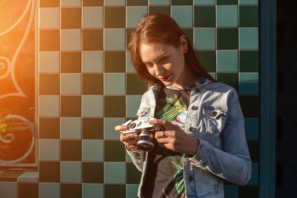 Cooles lustiges Mädchenmodel mit Retro-Filmkamera in Jeansjacke, dunkle Haare im Freien über der Stadtmauer im Käfighintergrund. Sonneneruption — Stockfoto