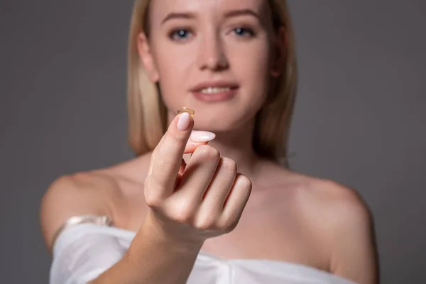 Focus on contact lens on finger of young woman. Young woman holding contact lens on finger in front of her face. Woman holding contact lens on grey background.