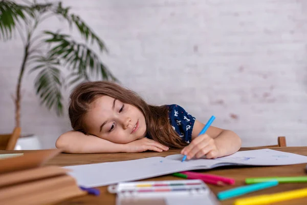 Inspiriertes kleines Mädchen am Tisch zeichnet mit Buntstiften oder erledigt Hausarbeit — Stockfoto