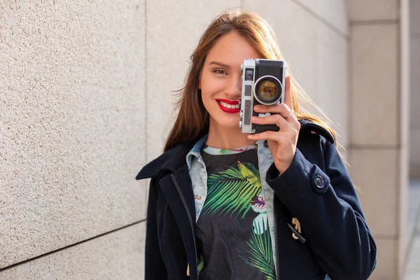 Счастливая девушка-хипстер делает фото ретро-камерой на городской улице — стоковое фото