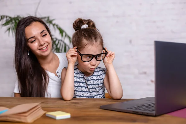 Привлекательная молодая женщина и ее маленькая милая дочь сидят за столом и веселятся, выполняя домашнее задание вместе . — стоковое фото