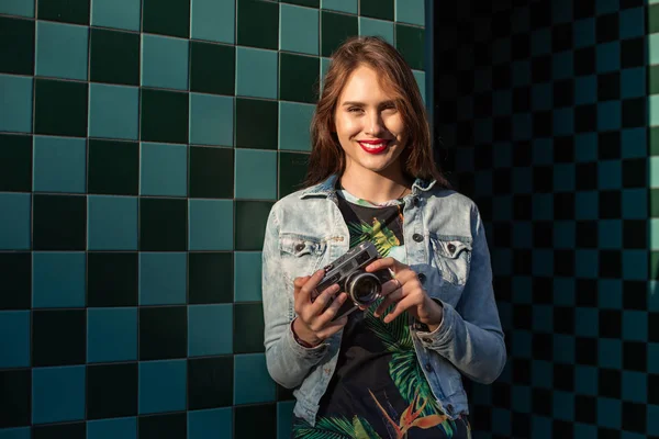 Cooles lustiges Mädchenmodell mit Retro-Filmkamera in Jeansjacke, dunkle Haare im Freien über der Stadtmauer im Käfighintergrund — Stockfoto