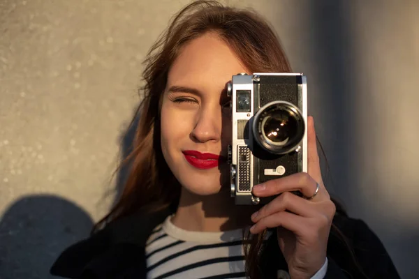 Lächelnde Fotografin in Jacke, die vor der Wand steht und bereit ist, ein neues Foto zu machen. — Stockfoto