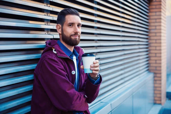 Όμορφος νεαρός άνδρας στο μωβ χειμερινό μπουφάν πίνοντας καφέ. Ο άνθρωπος που πίνει καφέ στην οδό. — Φωτογραφία Αρχείου