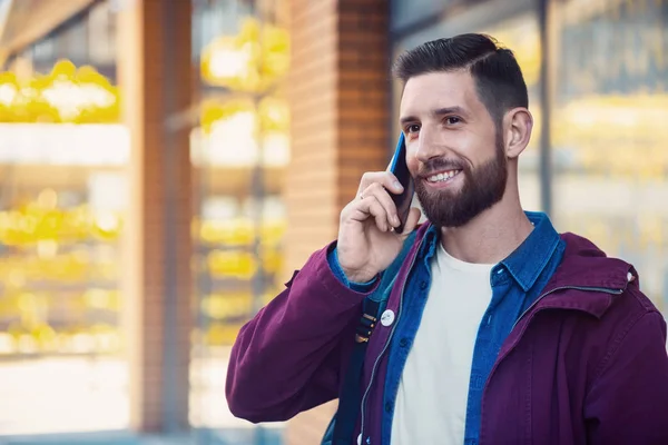 Joven vistiendo ropa de invierno con un smartphone en la mano, caminando por la calle. Bengala solar — Foto de Stock