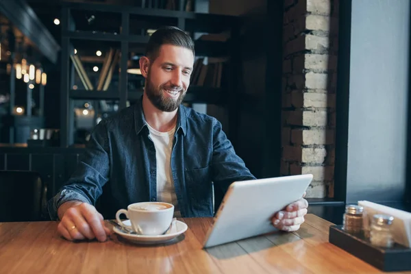 Hombre joven bebiendo café en la cafetería y el uso de tabletas — Foto de Stock