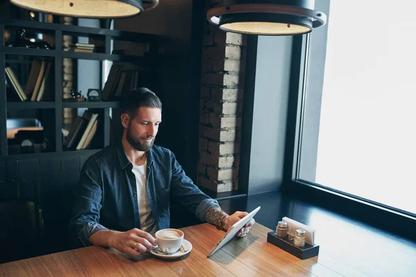 Hombre joven bebiendo café en la cafetería y el uso de tabletas — Foto de Stock