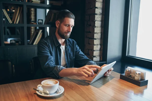 Hombre joven bebiendo café en la cafetería y el uso de tabletas — Foto de Stock