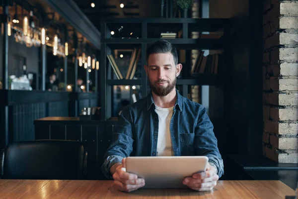Moderno empresario hipster tomando café en la cafetería de la ciudad durante el almuerzo y trabajando en la tableta — Foto de Stock