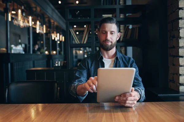 Moderno empresario hipster tomando café en la cafetería de la ciudad durante el almuerzo y trabajando en la tableta — Foto de Stock
