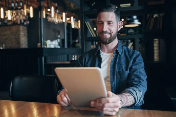 Moderno empresario hipster tomando café en la cafetería de la ciudad durante el almuerzo y trabajando en la tableta — Foto de Stock