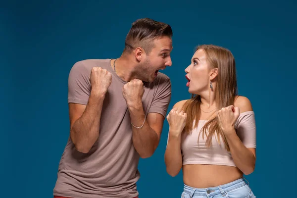 Mujer y hombre alegres levantan los puños con triunfo, tienen acuerdo exitoso, exclaman alegremente, sobre fondo azul . — Foto de Stock