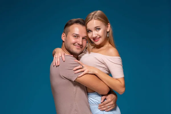 Casal jovem está abraçando em fundo azul no estúdio. Usam t-shirts, jeans e sorriem . — Fotografia de Stock