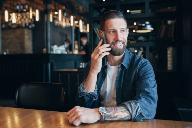 Arkadaşlarınızla konuşurken. Mobil telefonda konuşurken ve kafede otururken gülümseyen kendine güvenen genç adam