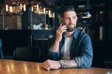 Cep telefonuyla konuşan ve kafede otururken gülümseyen kendine güvenen genç adam.