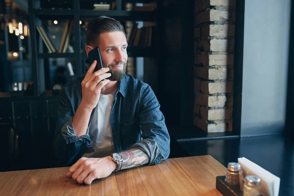 Confident young man talking on the mobile phone and smiling while sitting in cafe