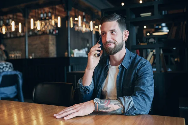 Confident young man talking on the mobile phone and smiling while sitting in cafe