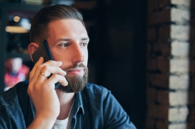 Cep telefonuyla konuşan ve kafede otururken gülümseyen kendine güvenen genç adam.
