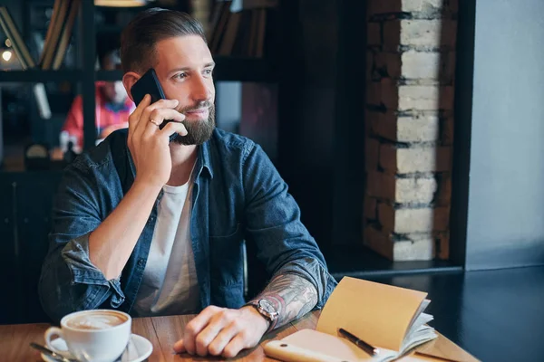 Confident young man talking on the mobile phone and smiling while sitting in cafe