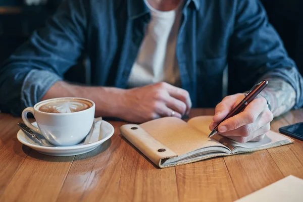 Mão de homem com caneta escrita em caderno em uma mesa de madeira. Close-up — Fotografia de Stock