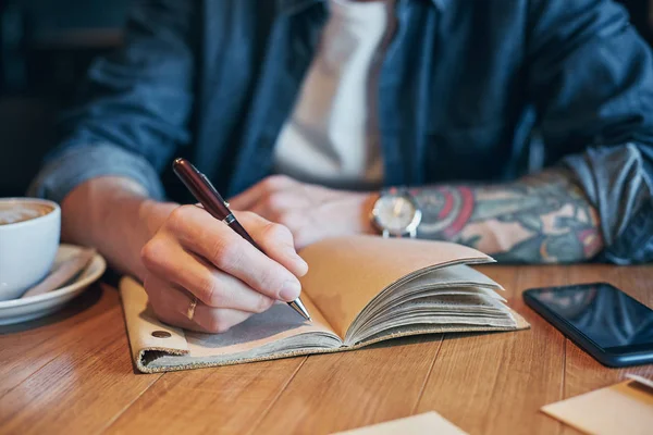 Man hand met pen schrijven op een notitieblok op een houten tafel. Close-up — Stockfoto