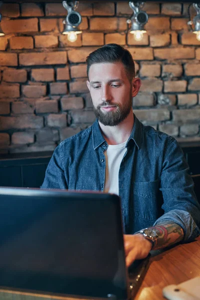 Joven guapo trabajando en el ordenador portátil mientras disfruta del café en la cafetería — Foto de Stock