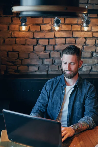 Joven guapo trabajando en el ordenador portátil mientras disfruta del café en la cafetería — Foto de Stock
