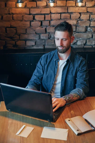 Schöner junger Mann arbeitet am Laptop, während er Kaffee im Café genießt — Stockfoto
