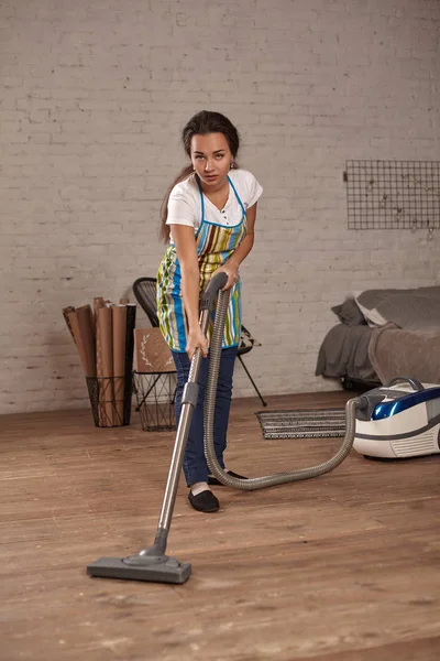 Giovane donna che utilizza l'aspirapolvere in casa pavimento del soggiorno, facendo compiti di pulizia e faccende, interni meticolosi . — Foto Stock