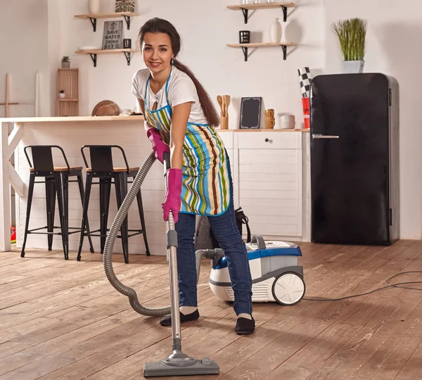 Mujer joven que usa aspiradora en el piso de la cocina casera, haciendo tareas de limpieza y tareas, interior meticuloso . — Foto de Stock