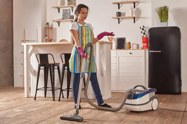 Mujer joven que usa aspiradora en el piso de la cocina casera, haciendo tareas de limpieza y tareas, interior meticuloso . — Foto de Stock