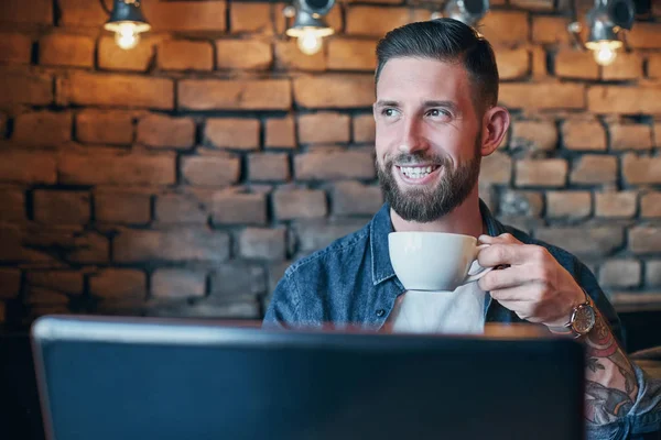 Hombre joven bebiendo café en la cafetería de la ciudad durante el almuerzo y trabajando en el ordenador portátil — Foto de Stock