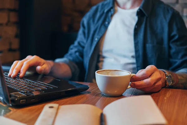 Mladý muž popíjel kávu v kavárně města v době oběda a práci na notebooku. Detailní záběr — Stock fotografie