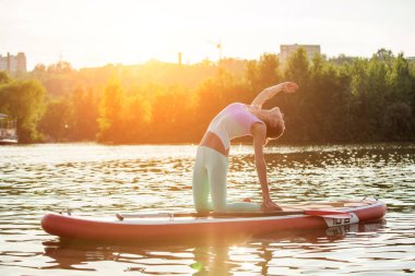 Genç kadın Yoga sup tahta üzerinde kürek ile yapıyor. Yoga poz, yan görünümü - doğa ile uyum kavramı.