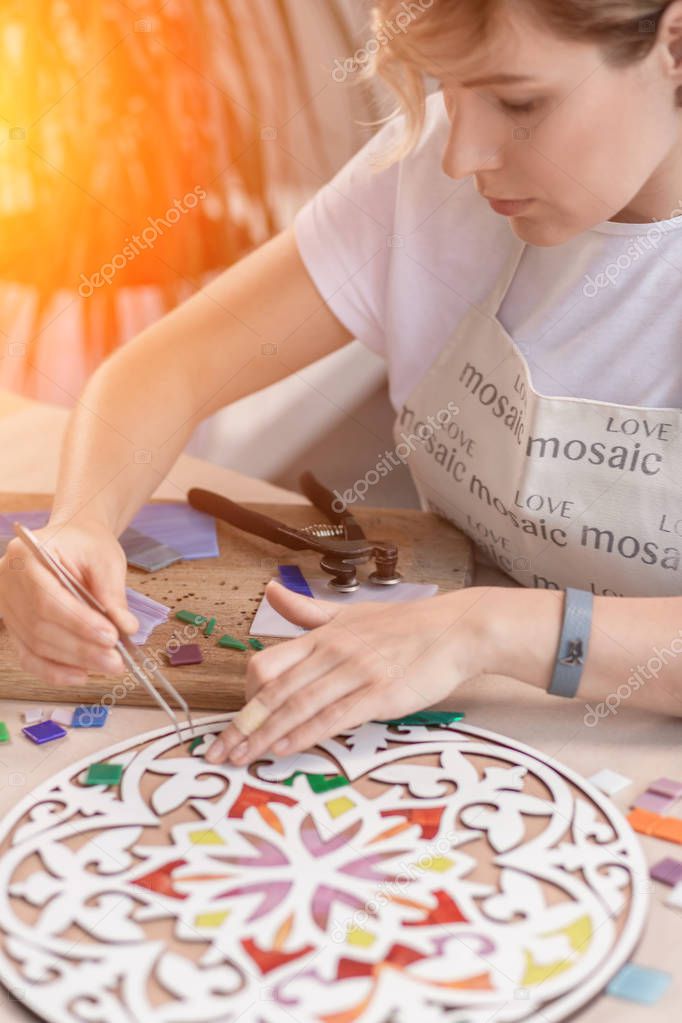 Workplace of the mosaic master: womens hands holding tool for mosaic details in the process of making a mosaic