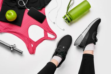 Cep telefonu, kulaklık, havlu ve fitness Club bir shaker çevrili bir hasır üzerinde oturan siyah eğitmenler giyen kızlar bacaklar. Üstten Görünüm.