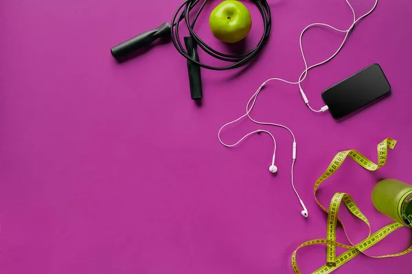 Health fitness background. Sneakers, dumbbell, power grip, green apple, water bottle, blue shirt, phone and earphone on dark background.