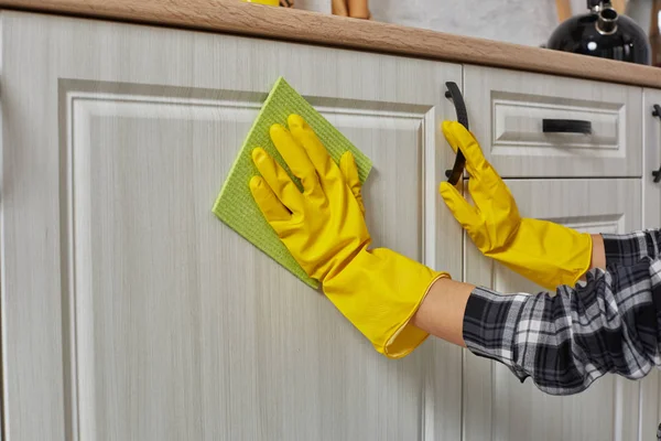 Mani in guanti con straccio verde sta pulendo armadi da cucina - lavori domestici e concetto di pulizia — Foto Stock