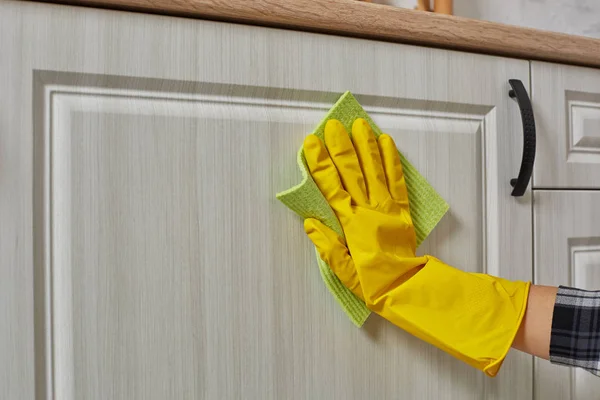 Mani in guanti con straccio verde sta pulendo armadi da cucina - lavori domestici e concetto di pulizia — Foto Stock