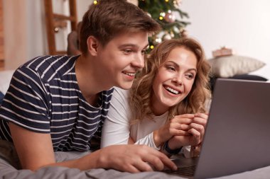 Gülümseyen genç çift erkek ve kadın yatakta yatan ve laptop bir şey izliyor