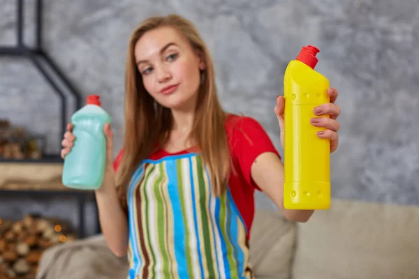 Vrouw vergelijkt twee wasmiddel fles thuis reiniging in een woonkamer. Thuiswerk. — Stockfoto