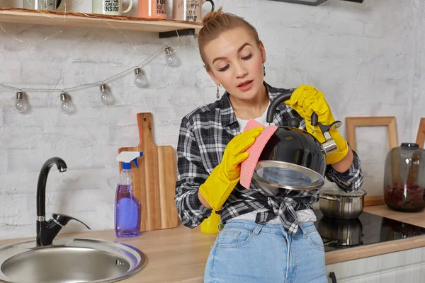 Domestic service and housekeeping concept, happy blonde lady cleaning kitchen kettle.